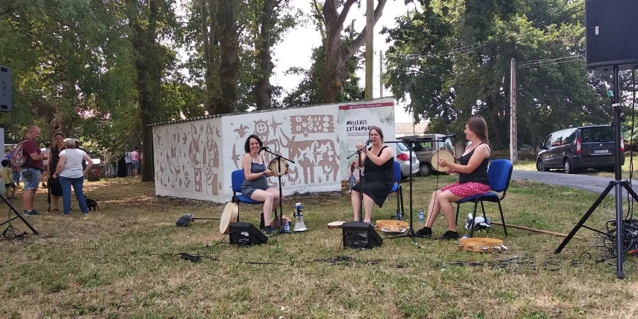 Tres pandeireteiras tocan nun campo, diante dun muro pintado